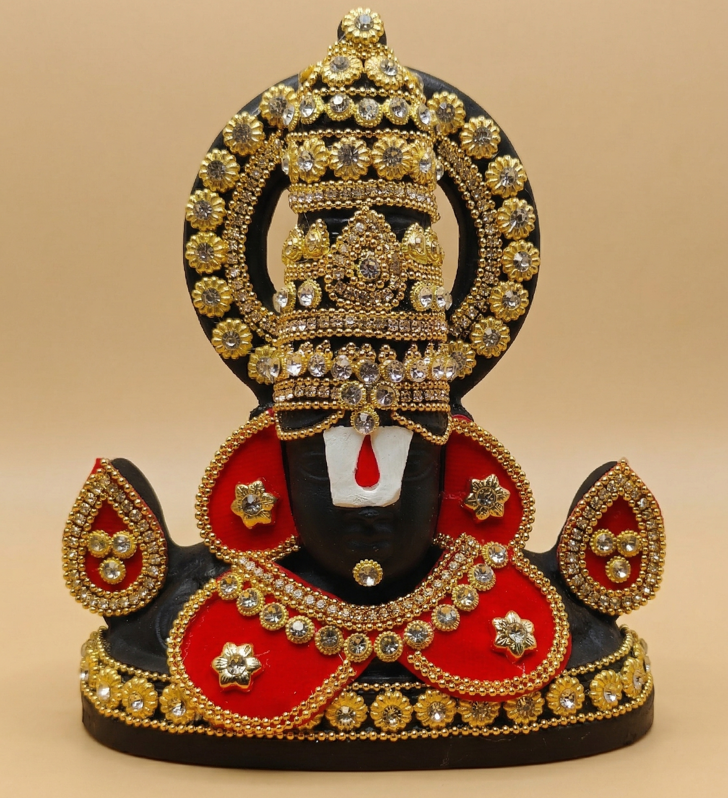 Black Tirupati Balaji divine face adorned with red and gold-tone stone embellishments on a beige background