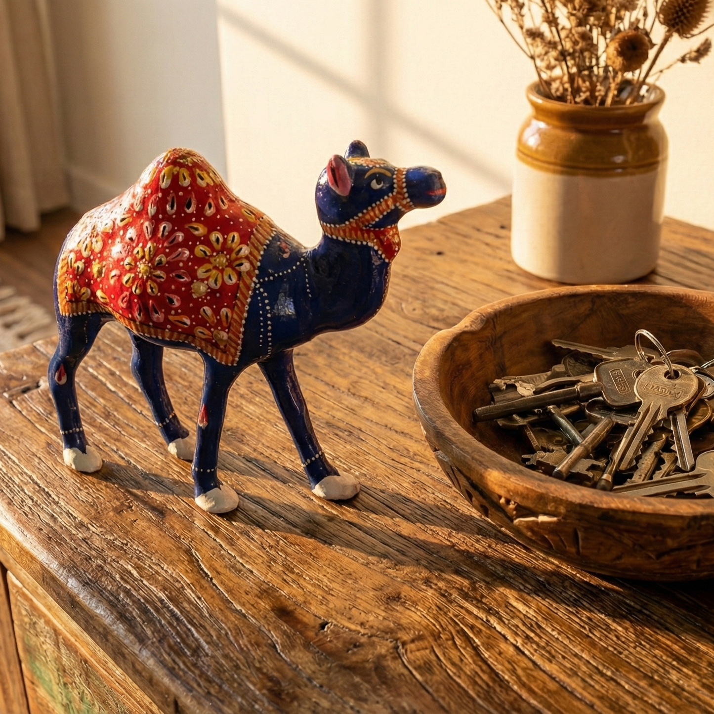 Decorative Meenakari Metal Camel figurine next to a bowl of keys on a wooden surface.