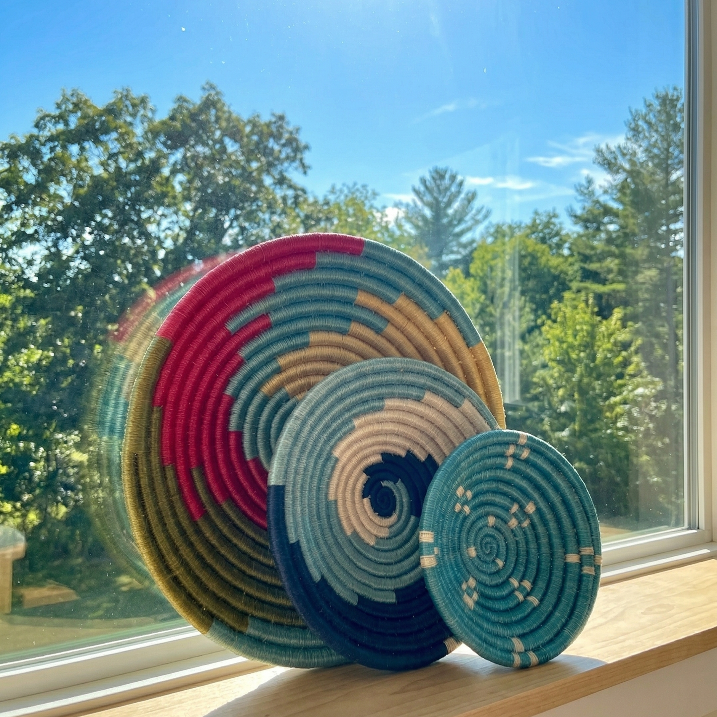 Set of assorted colorful Sabai grass handwoven baskets featuring vibrant geometric and spiral patterns near the window