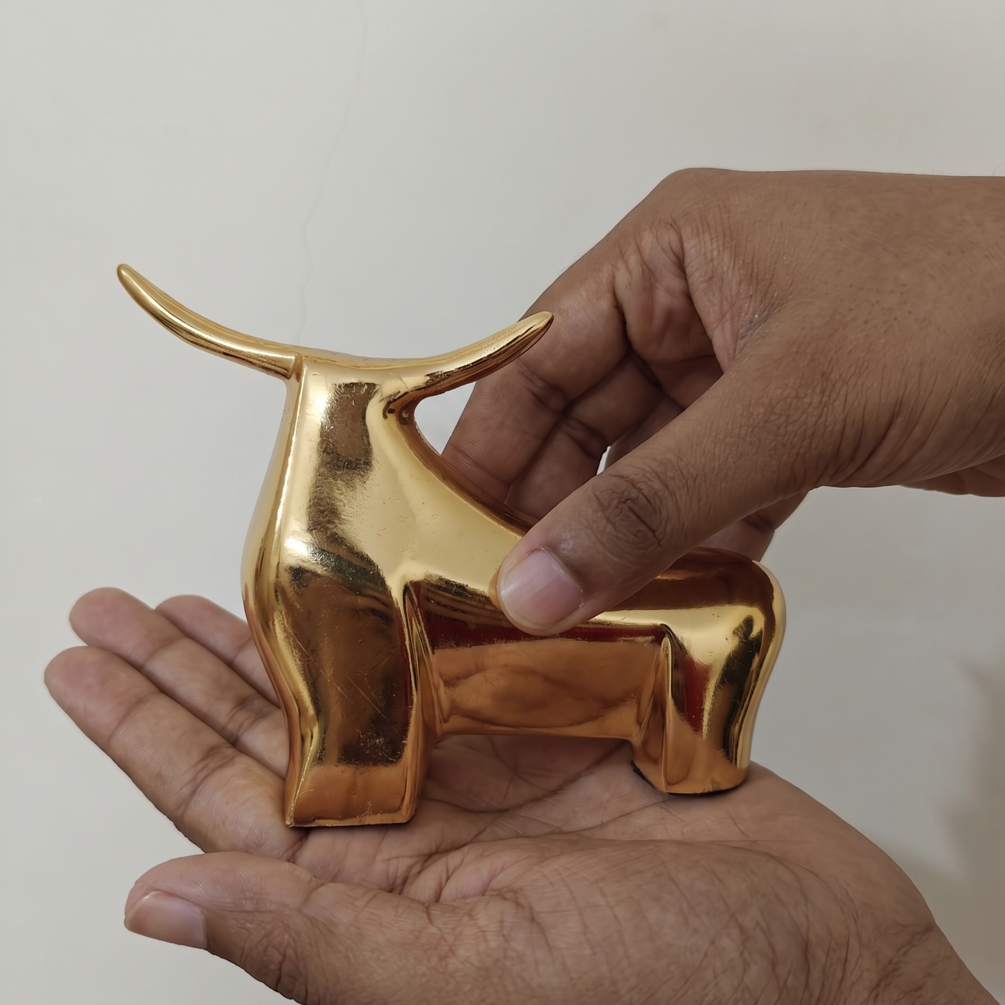 A close-up showing a clean hand placing the entire bull figurine (horns and body) into the palm of the other hand. This provides immediate, non-abstract proof of its small footprint.