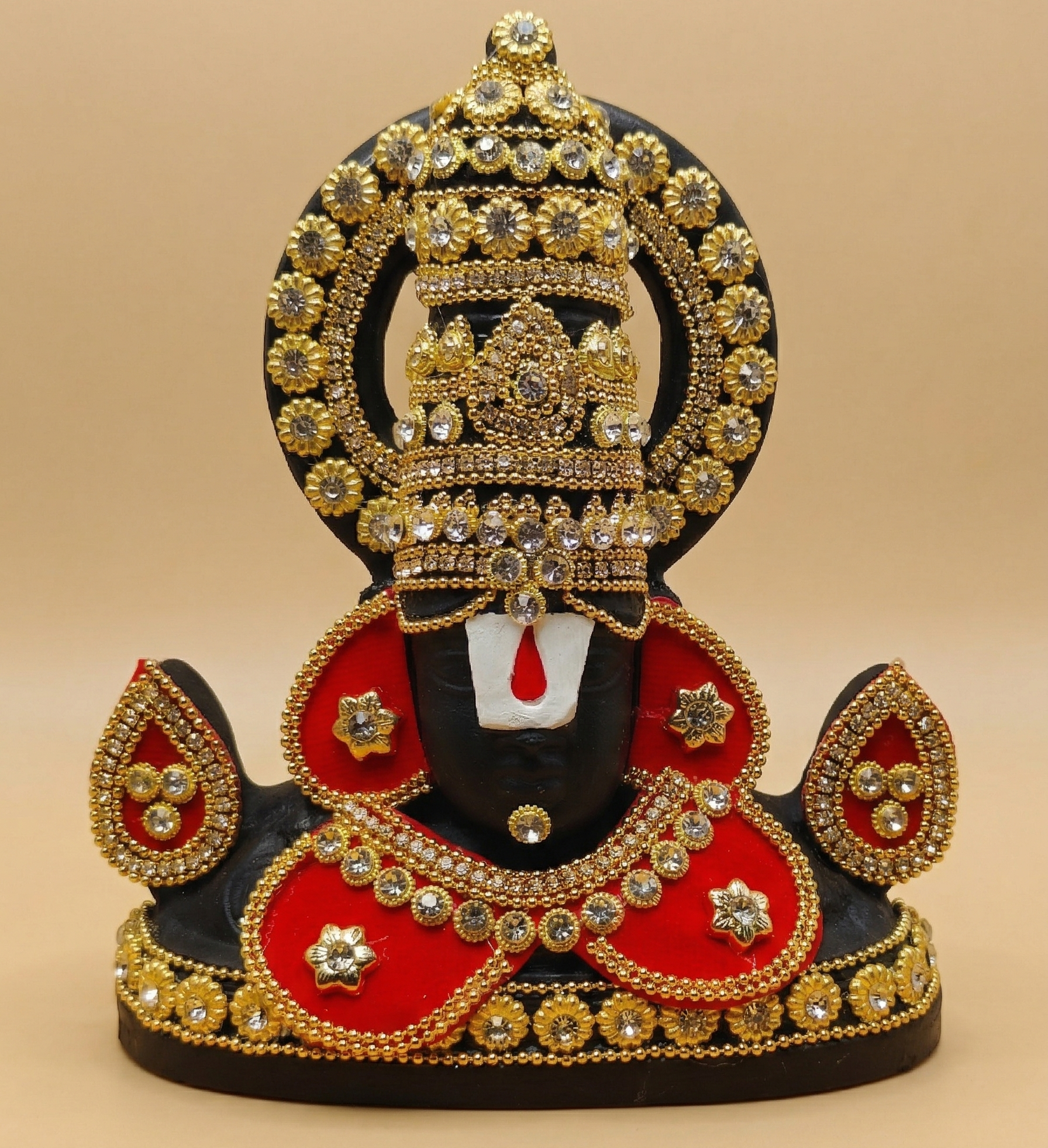 Black Tirupati Balaji divine face adorned with red and gold-tone stone embellishments on a beige background