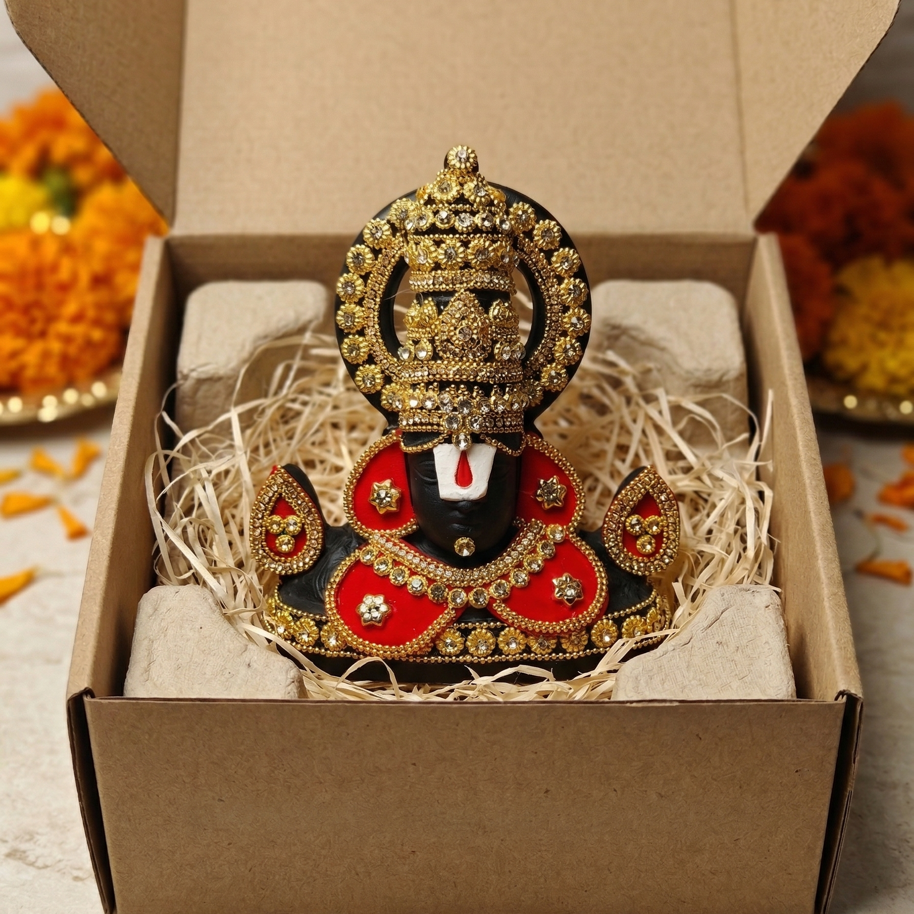 Black Tirupati Balaji divine face adorned with red and gold-tone stone embellishments packed in a box for gifting