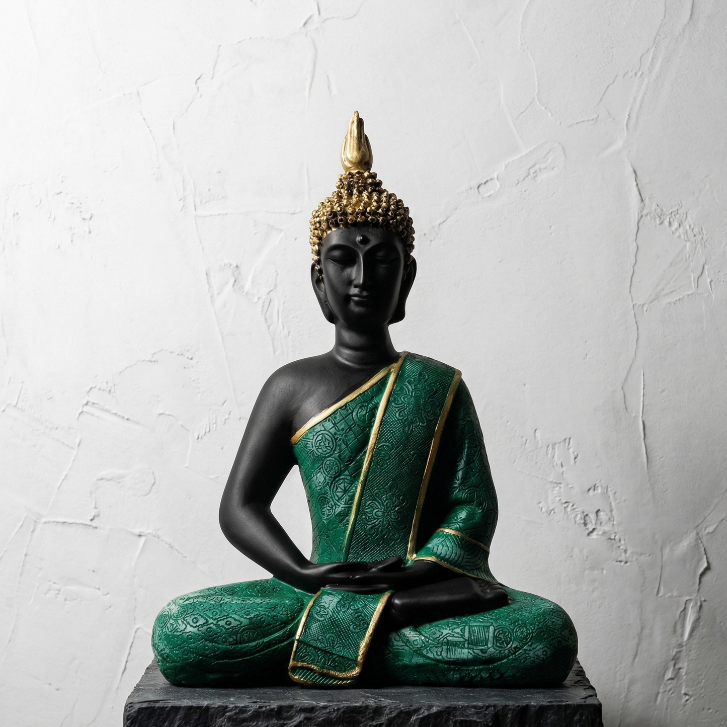 Black meditating Buddha statue in Dhyana mudra wearing intricately textured green robe with gold borders placed on a black stone dim light