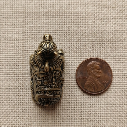 A highly detailed, miniature metal Nandiji figurine with a darkened antique finish placed directly next to a US penny for scale on a textured beige fabric.