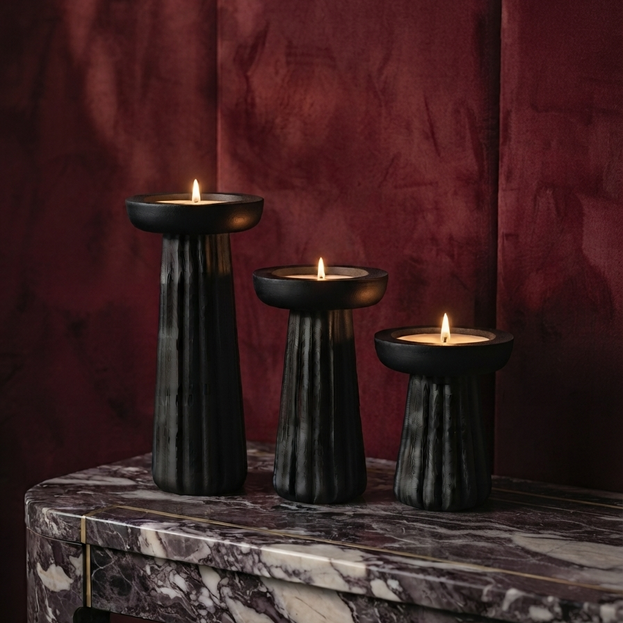 Three lit tealight candles placed in black carved wooden holders of descending heights, sitting on a luxurious purple marble console table against a deep burgundy velvet wall.