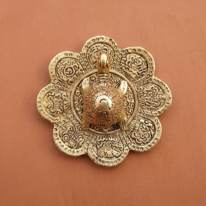 Top-down close-up of a detailed gold-polished aluminum tortoise figurine resting on a matching embossed mandala plate, set against a smooth terracotta background.