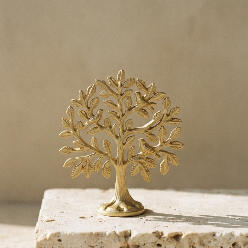 A detailed gold-polished aluminum tree of life resting on a block of porous travertine stone against a smooth, neutral beige background in bright sunlight.