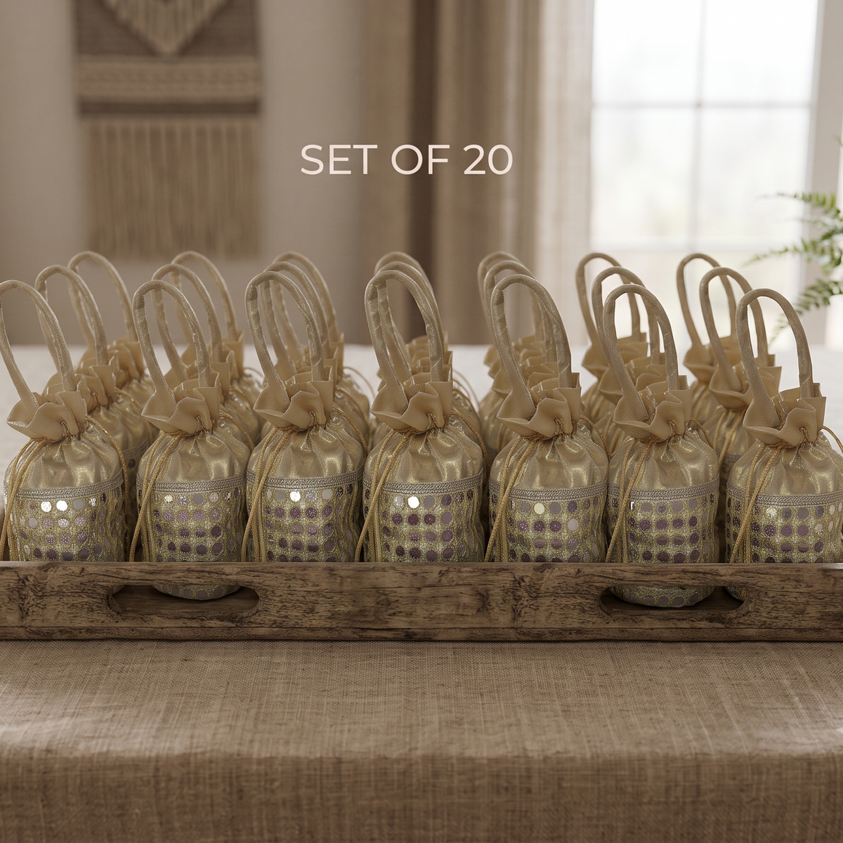large rustic wooden tray neatly filled with twenty golden mirror-work potli bags, arranged as elegant event favors on a linen-covered table.
