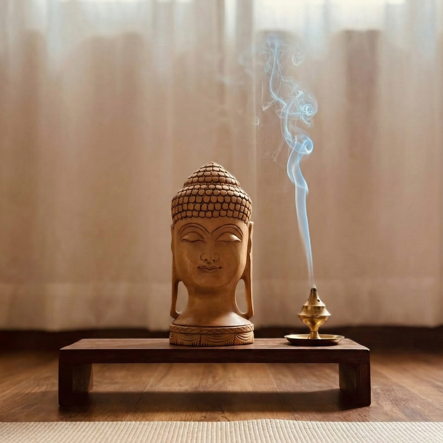 Hand-carved wooden Buddha head sculpture with incense on a wooden platform against a curtain backdrop