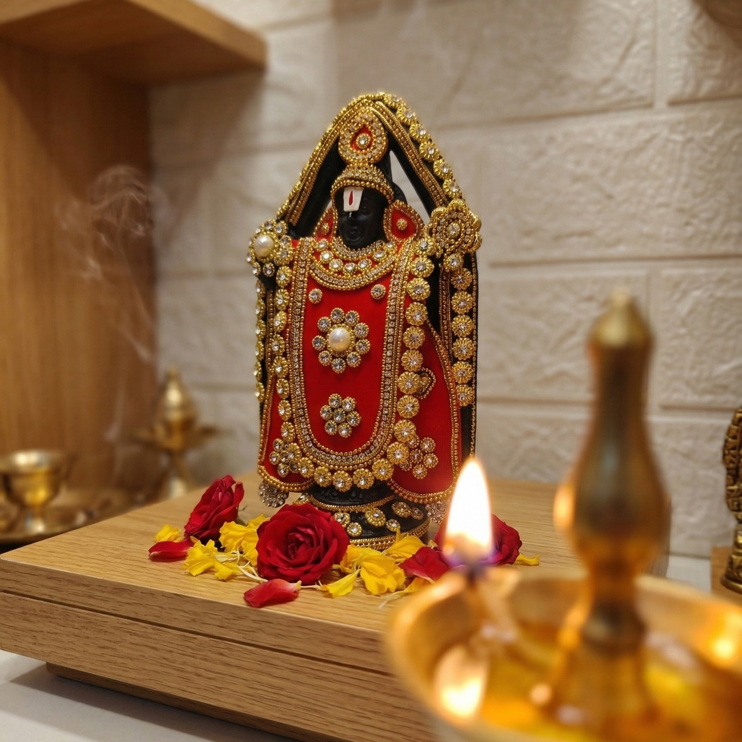 Handcrafted black Lord Venkateswara (Tirupati Balaji) murti richly adorned with red fabric, gold-tone detailing, and sparkling stones placed in a home temple
