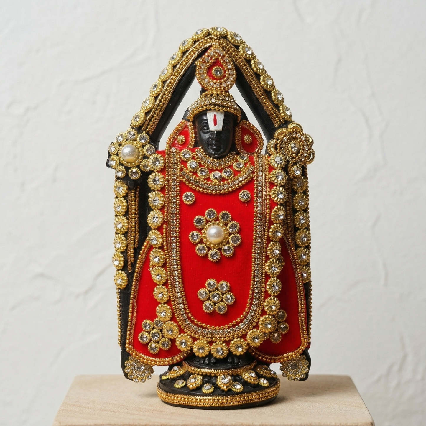 Handcrafted black Lord Venkateswara (Tirupati Balaji) murti richly adorned with red fabric, gold-tone detailing, and sparkling stones.