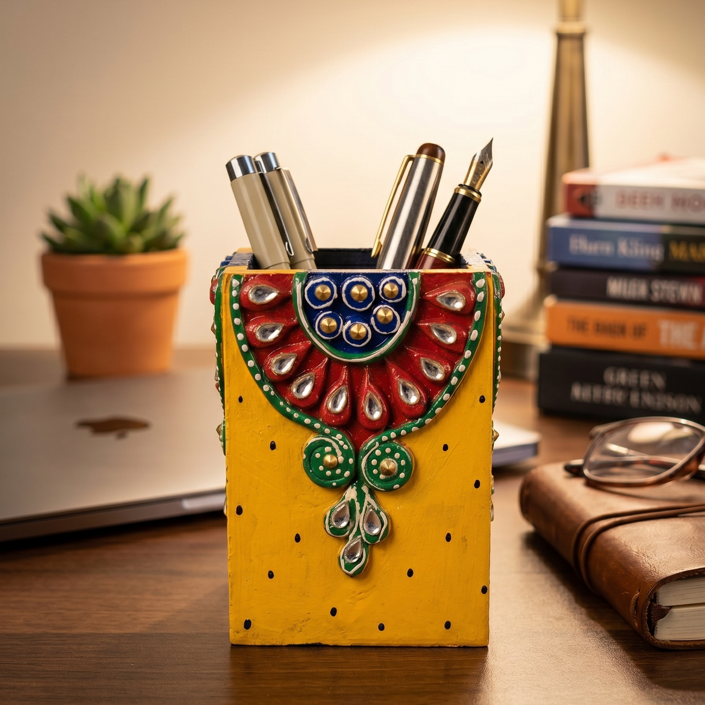 Handcrafted wooden pen holder in bright yellow, decorated with traditional kundan mirror work placed on a study table with pens inside it