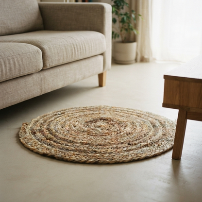 A large 23-inch braided golden jute mat utilized as a small organic floor rug, placed on a smooth light floor next to a cozy beige sofa and a wooden coffee table.