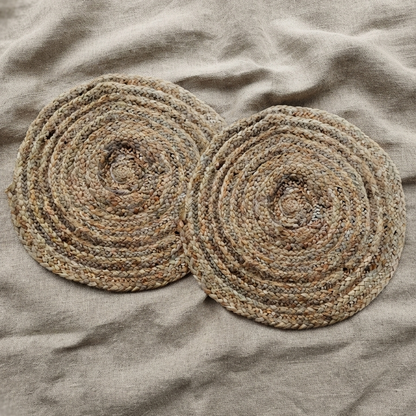 Top-down view of two round braided natural golden jute mats overlapping each other, displayed flat to highlight their twisted fibers on a textured beige linen fabric background.
