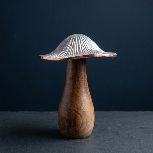 Close-up of a decorative mushroom featuring a polished wooden stem and a finely textured silver metal cap, displayed on a dark, rough slate tile against a deep navy blue background.