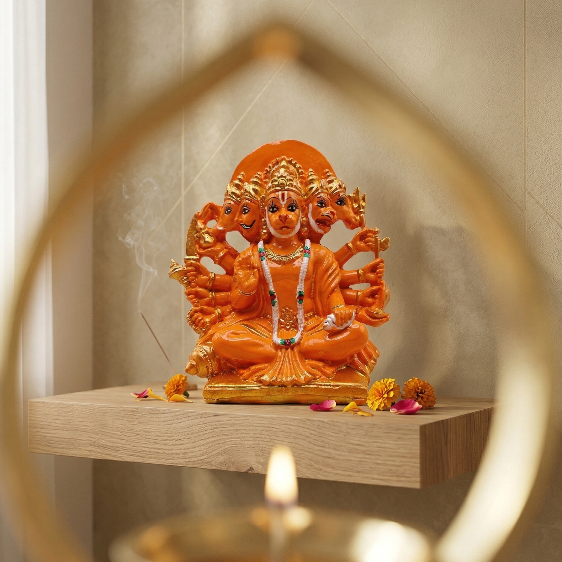 Orange Panchmukhi Hanumanji murti with five divine faces and ten arms, seated on a wooden shelf with a lit candle in the foreground.