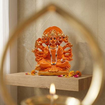 Orange Panchmukhi Hanumanji murti with five divine faces and ten arms, seated on a wooden shelf with a lit candle in the foreground.
