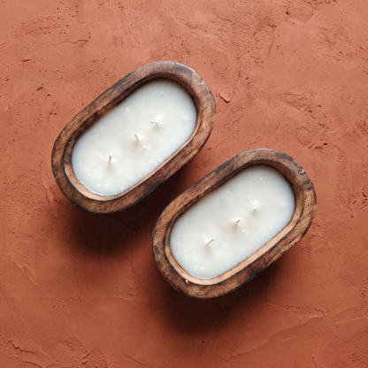 Top-down view of a set of two elongated oval 3-wick dough bowl candles with white wax, displayed diagonally on a warm, textured terracotta background.