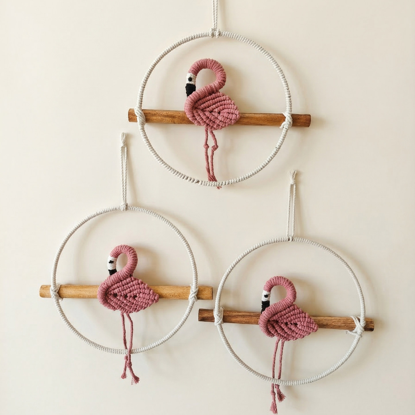 Set of 3 handcrafted macrame pink flamingo wall hangings sitting on wooden perches.