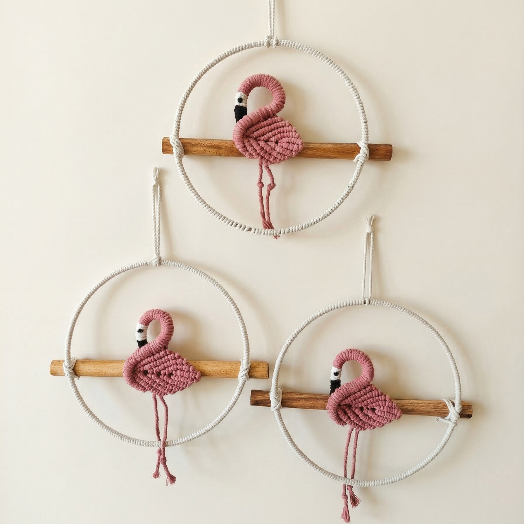 Set of 3 handcrafted macrame pink flamingo wall hangings sitting on wooden perches.