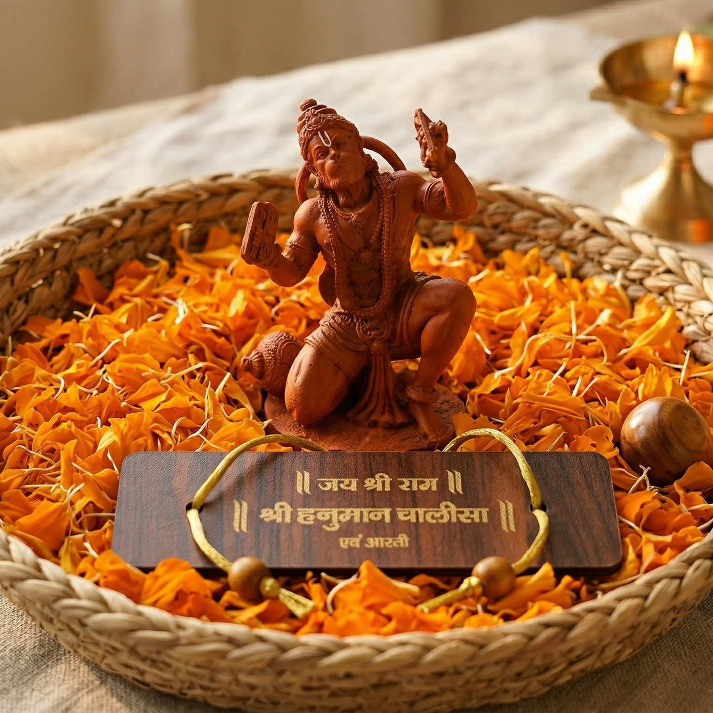 Sinduri Hanumanji statue and Hanuman Chalisa on a bed of marigold flowers in a woven basket, with a candle and additional flowers in the background