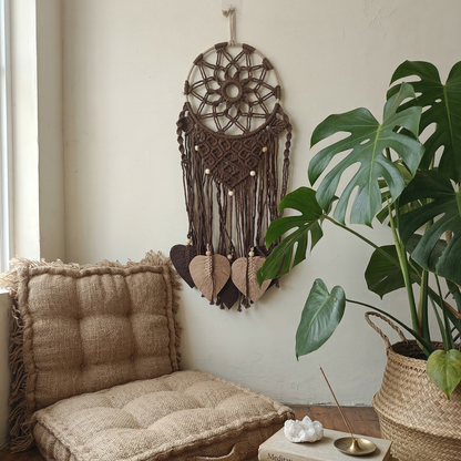 Cozy living room corner with a cushioned chair, dreamcatcher, and potted plant.