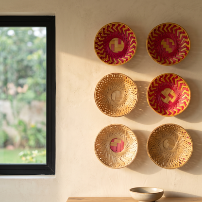 Six woven bamboo decorative bowls arranged symmetrically in two vertical columns on a beige textured wall beside a black-framed window.