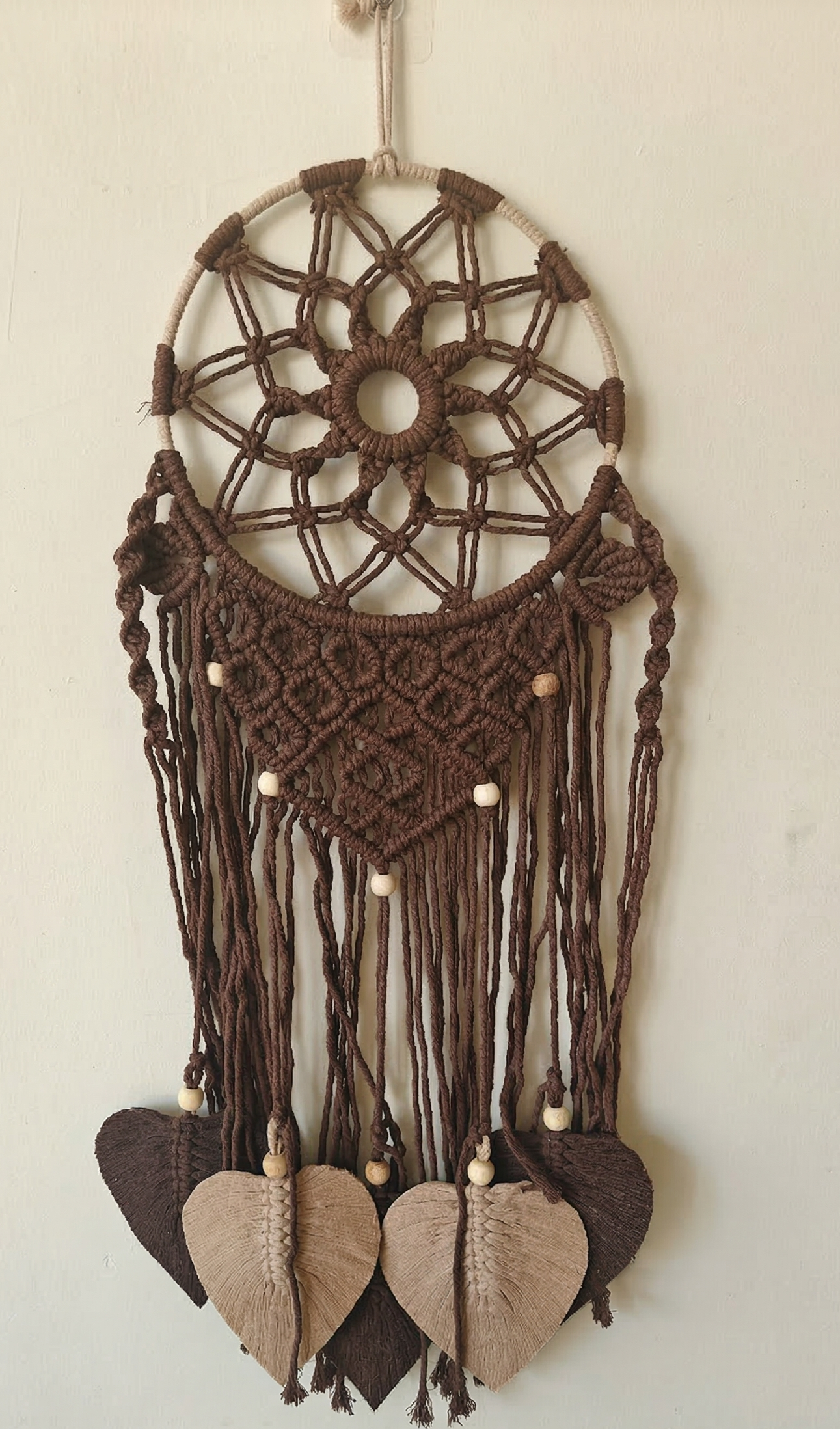 Brown dreamcatcher with leaf-shaped design on a beige background