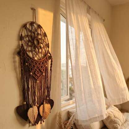 Dreamcatcher on a wall next to a window with sheer curtains.