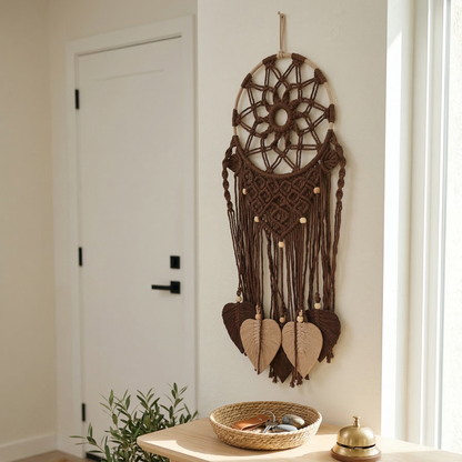 Brown dreamcatcher hanging on a white wall above a wooden table with a plant and small bowl.