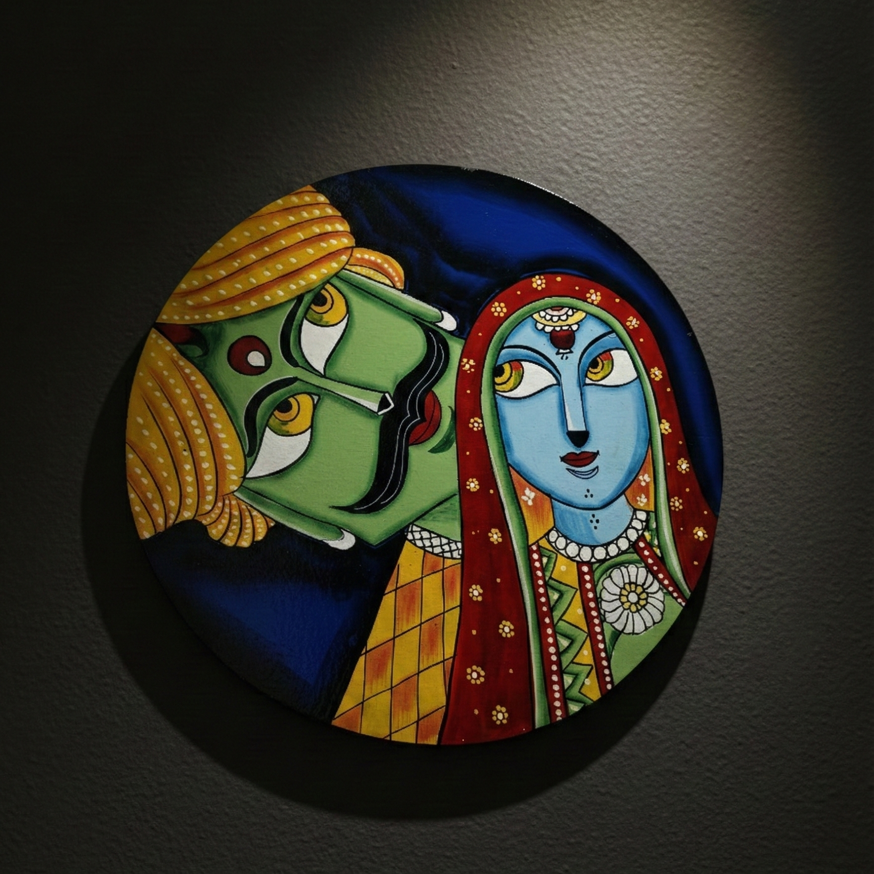 Round, hand-painted wooden wall plate featuring vibrant Rajasthani Kathputli puppet art of a man and woman, hanging on a dark wall as cultural decor.