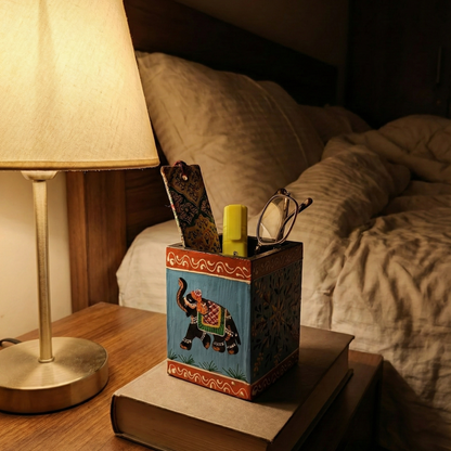 Blue hand-painted wooden elephant holder used as a bedside organizer on a wooden nightstand, holding eyeglasses and stationery 