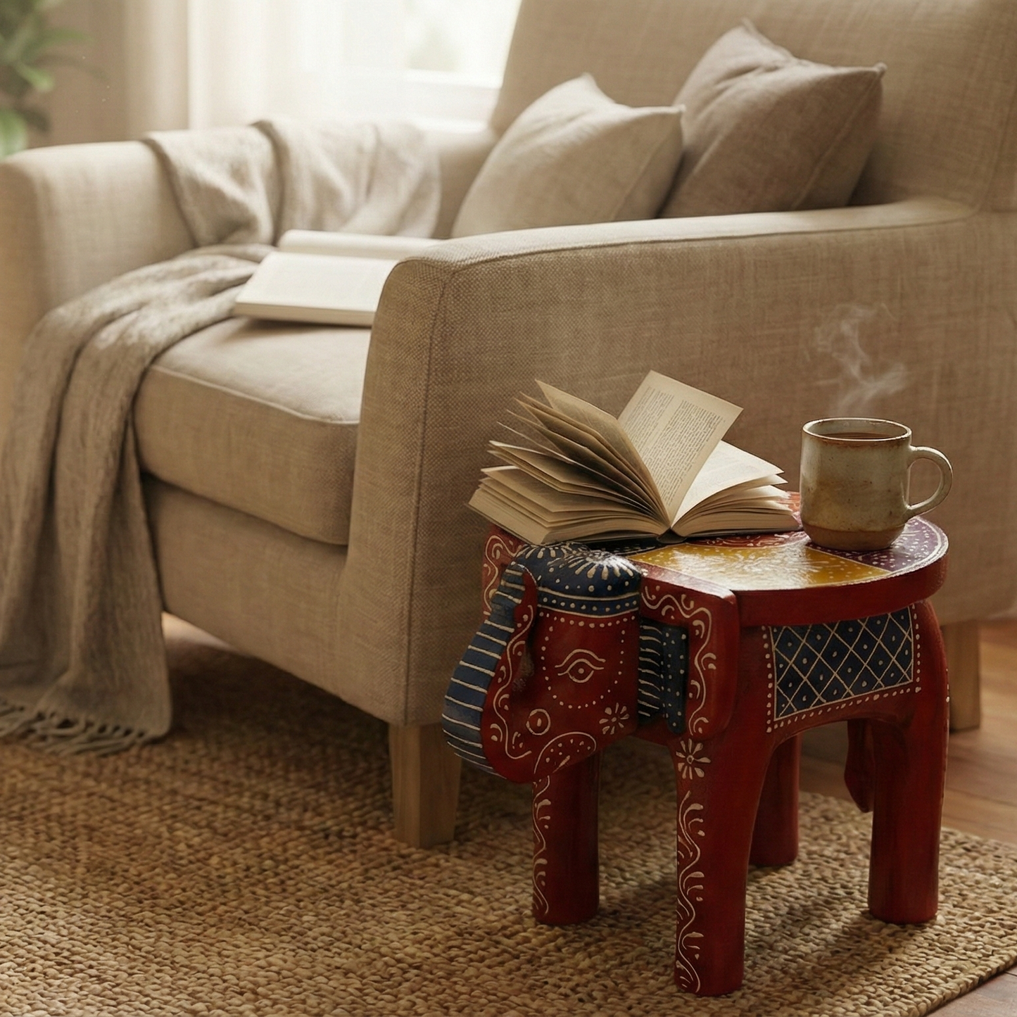 Red hand-painted wooden elephant stool used as a side table in a cozy reading corner. Styled with an open book and coffee mug next to a beige armchair