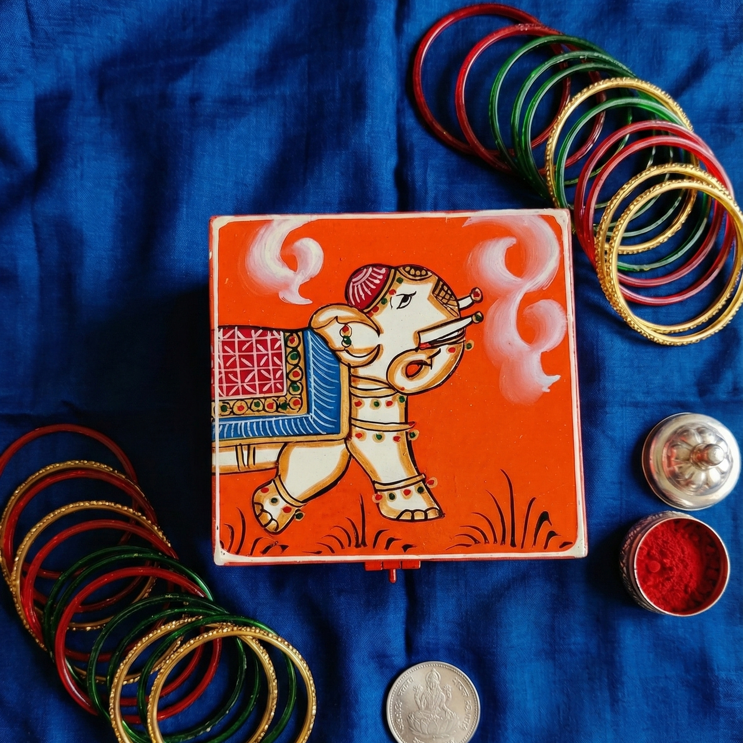 Orange hand-painted wooden storage box with traditional elephant art, used for jewelry and trinkets.