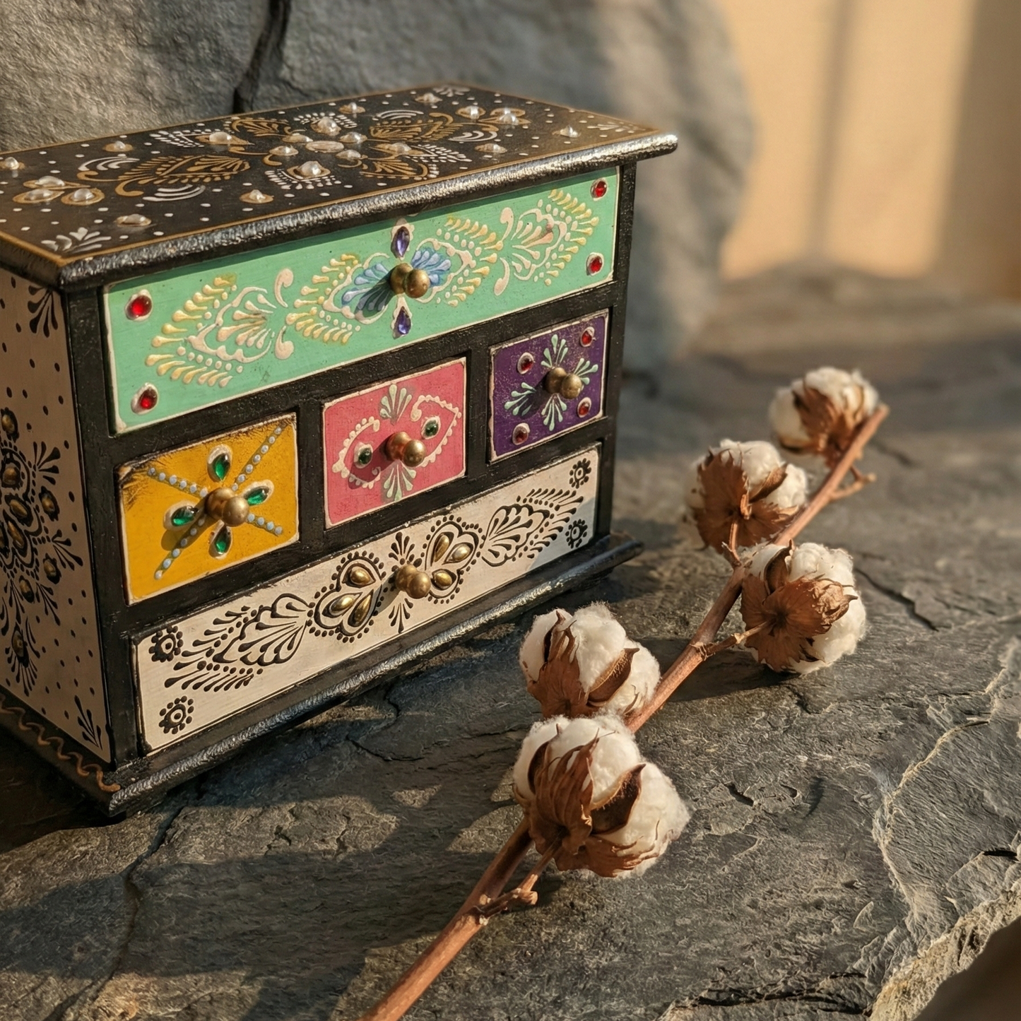 Hand-painted wooden mini chest with colorful drawers styled with dried cotton flowers on a stone surface for a rustic boho home decor look