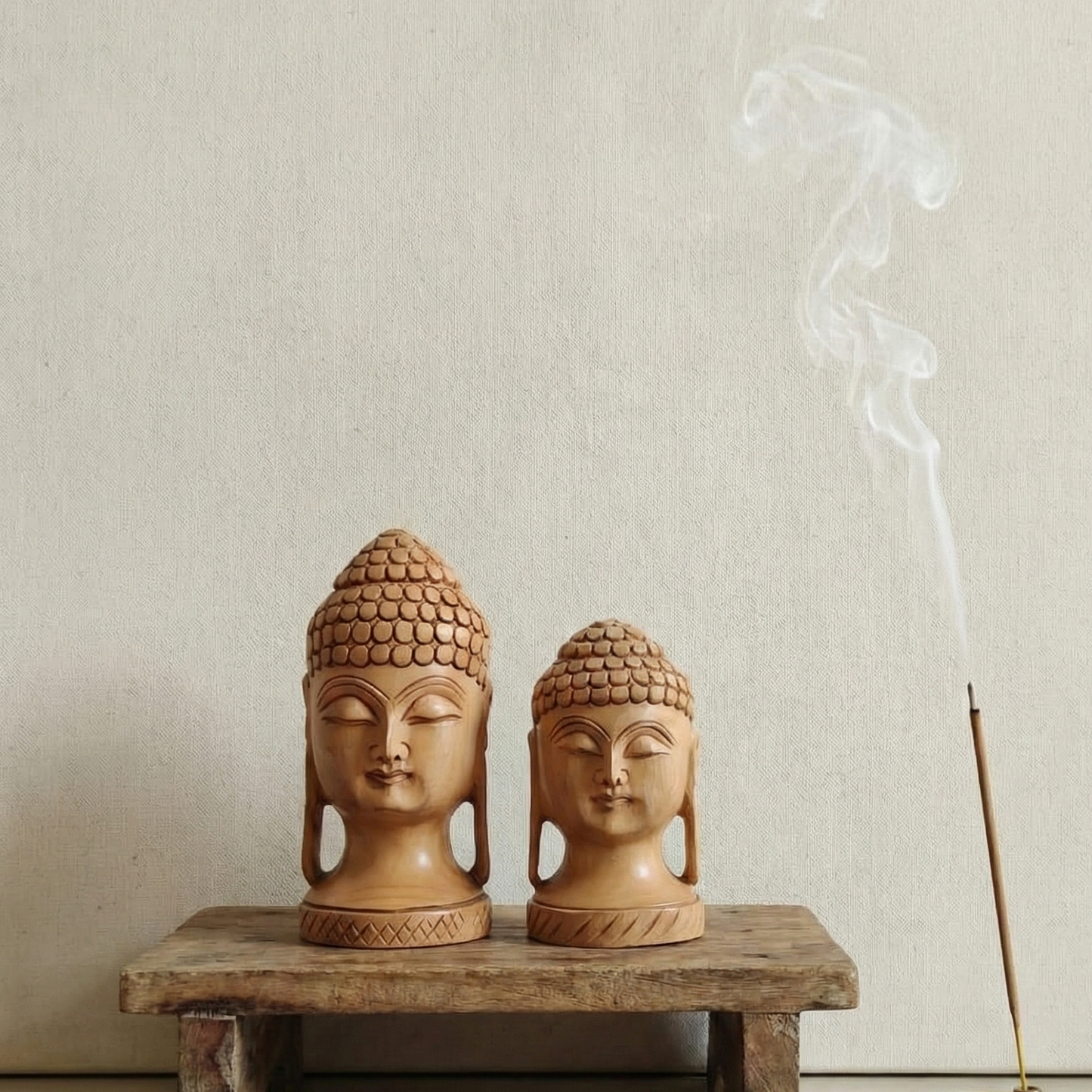 Minimalist meditation setup featuring a set of wooden Buddha heads on a rustic bench with burning incense smoke. Ideal for yoga studios and mindfulness corners.