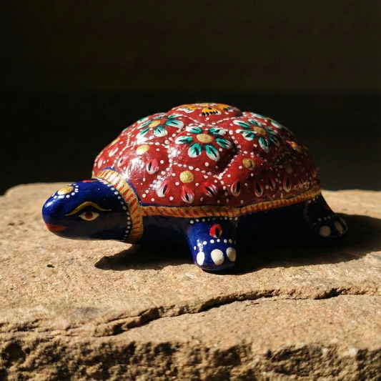Side profile view of the red metal Feng Shui tortoise figurine perched on a natural rock for good luck.