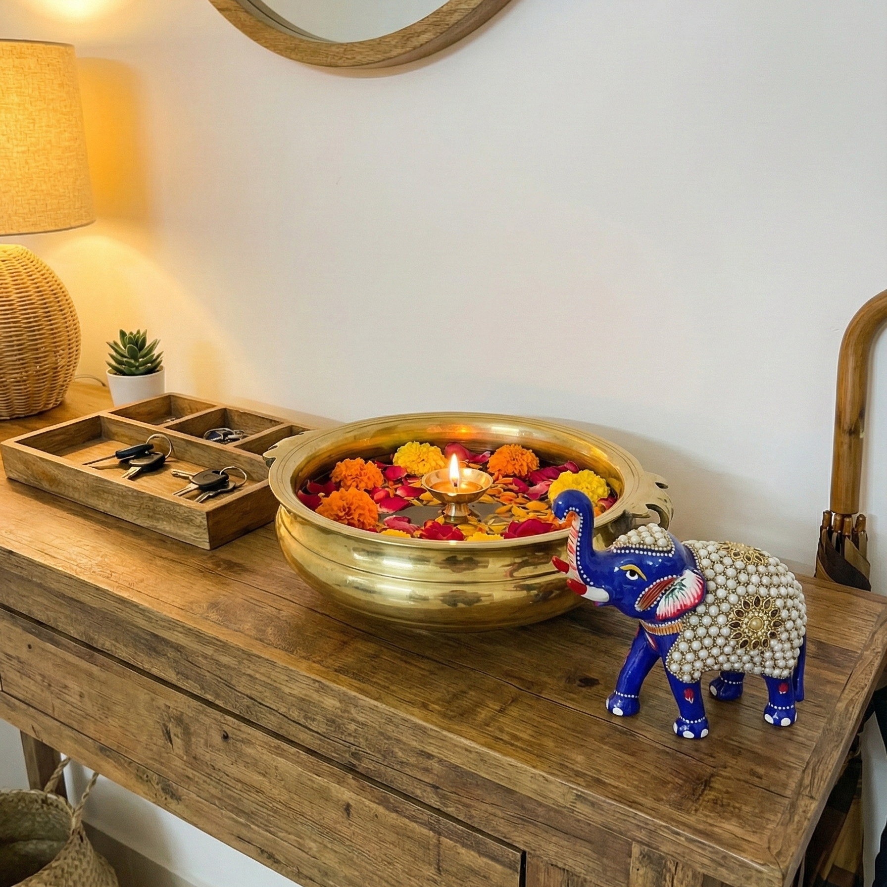 Blue Vastu elephant figurine displayed on a wooden console table next to a brass urli with flowers and candles, creating a welcoming traditional Indian entryway.