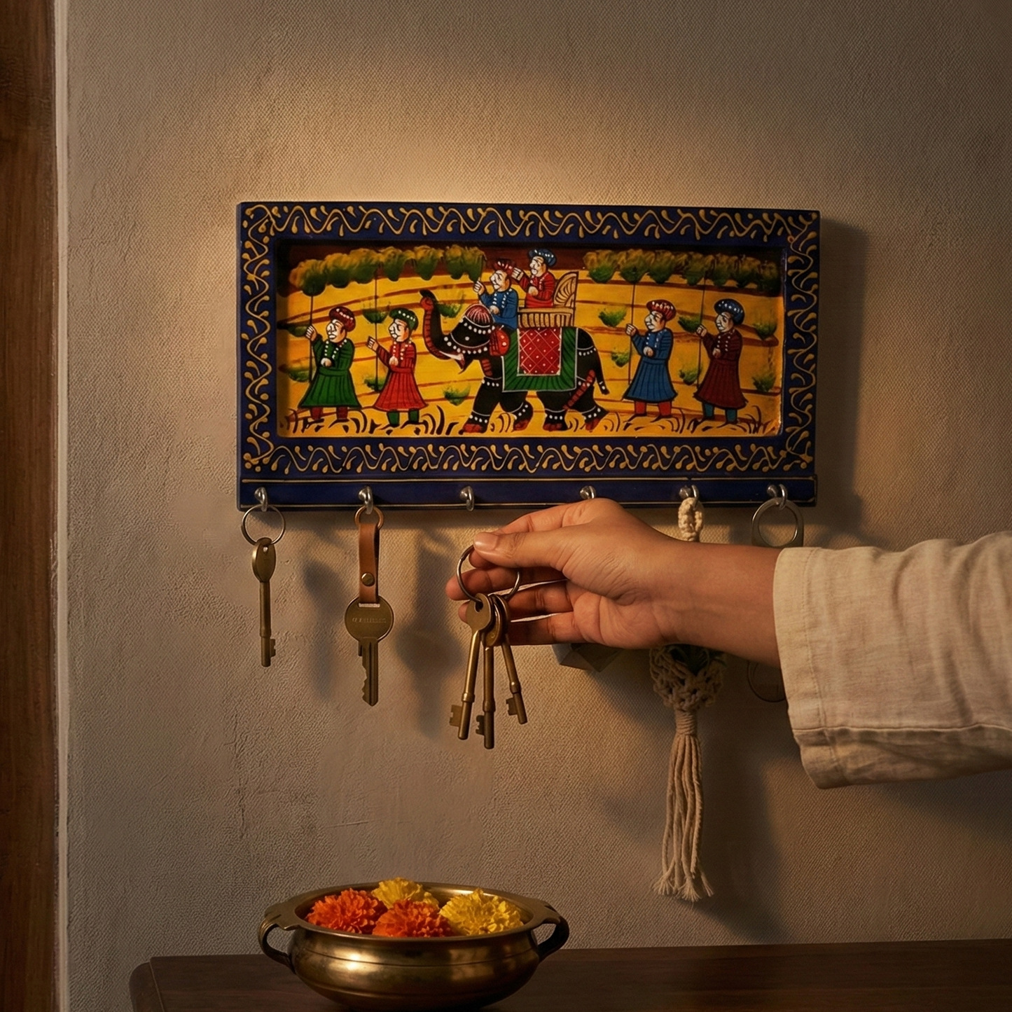A handcrafted blue wooden key holder for the wall featuring traditional Rajasthani elephant painting, hand reaching to hang keys.