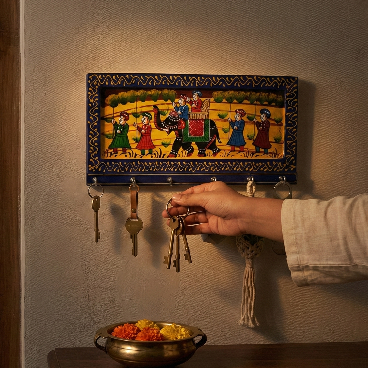 A handcrafted blue wooden key holder for the wall featuring traditional Rajasthani elephant painting, hand reaching to hang keys.